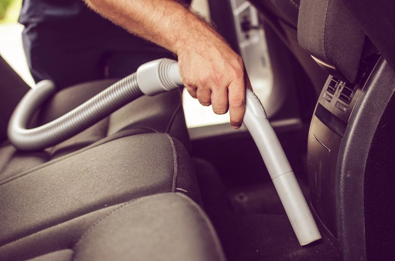 A person using an attachment to clean the seat of a car.